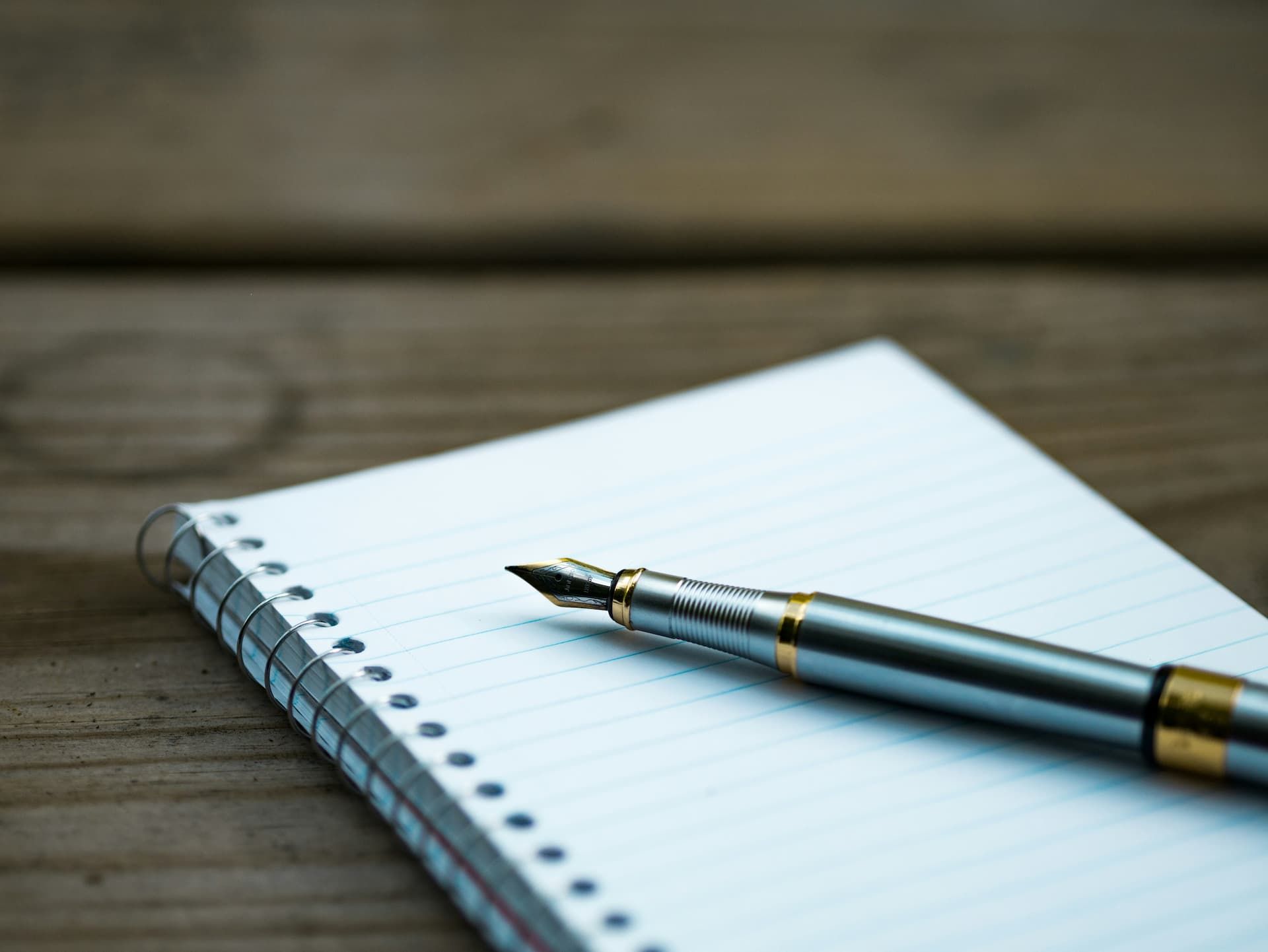 A pen is sitting on top of a notebook on a wooden table.