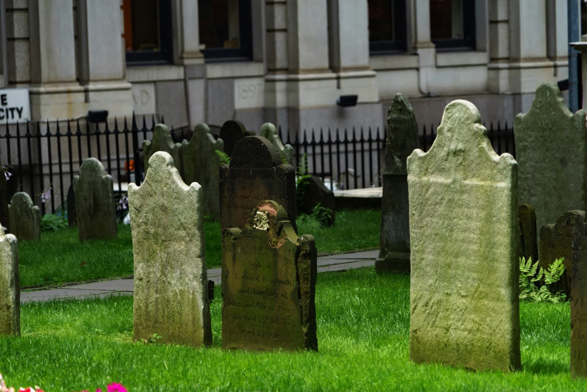 A cemetery with graves in the grass in front of a building.