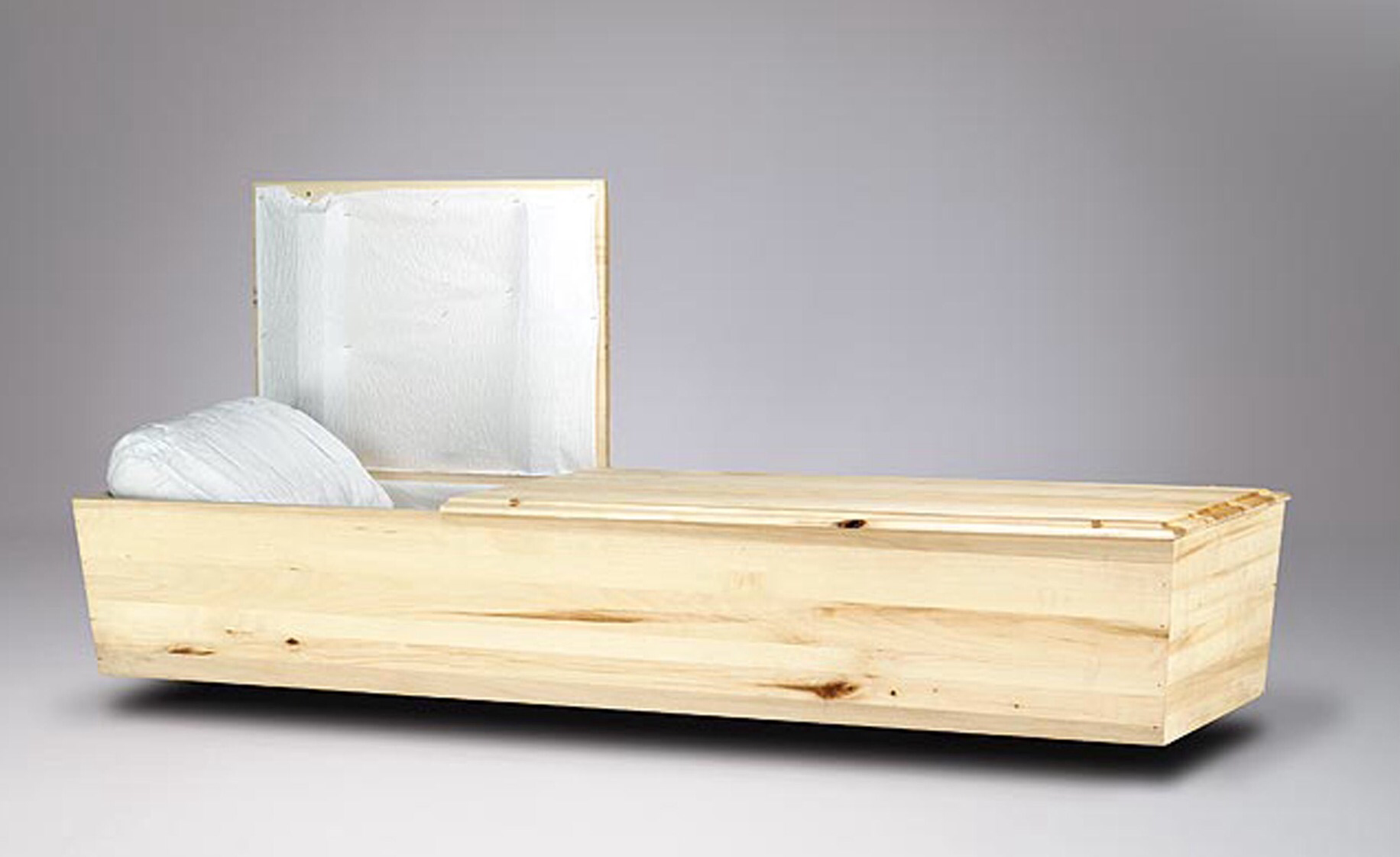 A wooden coffin with the lid open and a white blanket inside.