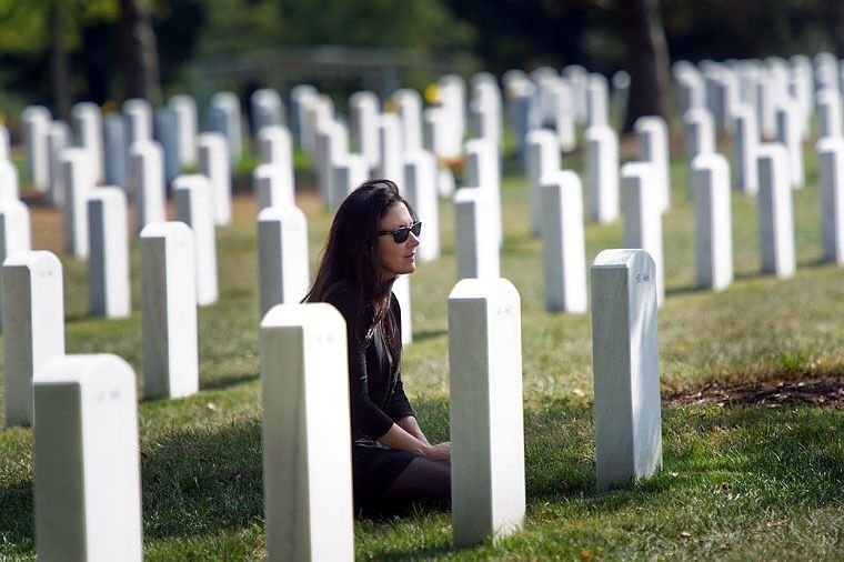 A woman is sitting in a cemetery surrounded by graves.