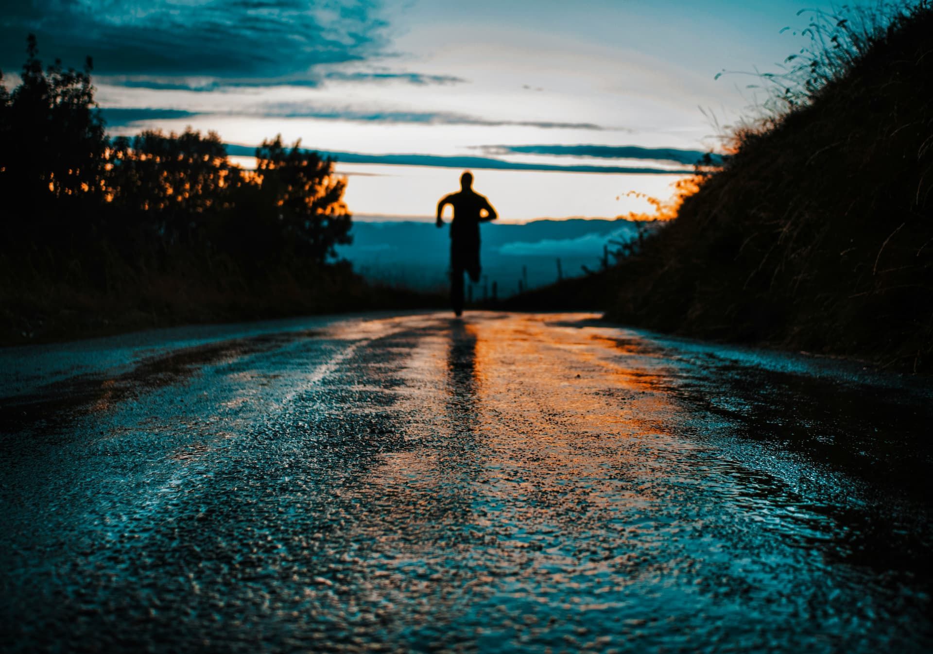 A man is running down a wet road at sunset.