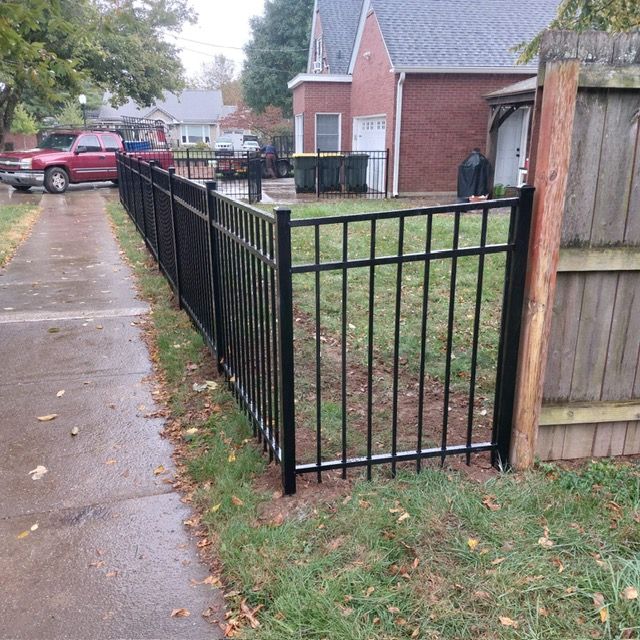 A black metal fence surrounds a grassy yard next to a wooden fence. | Louisville, KY | Lancaster Fencing