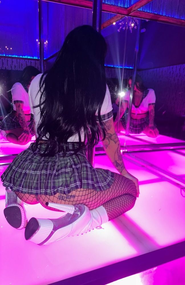 Woman in plaid skirt and fishnets kneels on a lighted stage, reflected in mirrors.