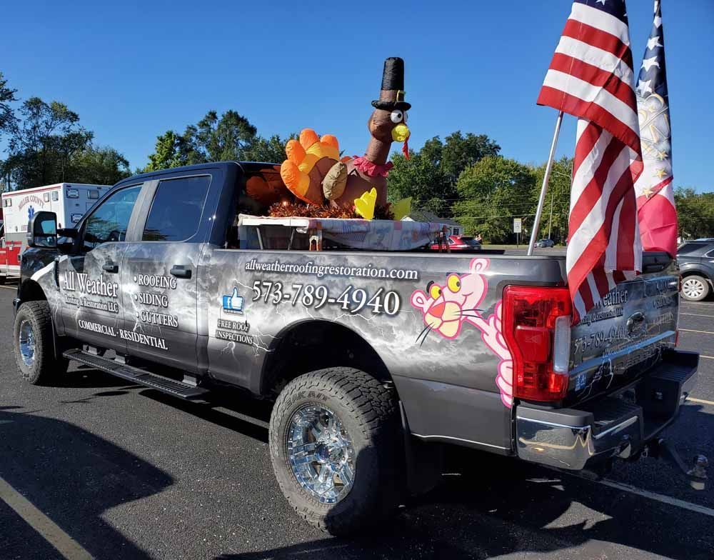 Gray pickup truck with turkey statue, American flags, and business logo.