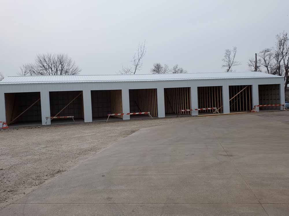 Row of unfinished storage units under a cloudy sky. Concrete drive in foreground.