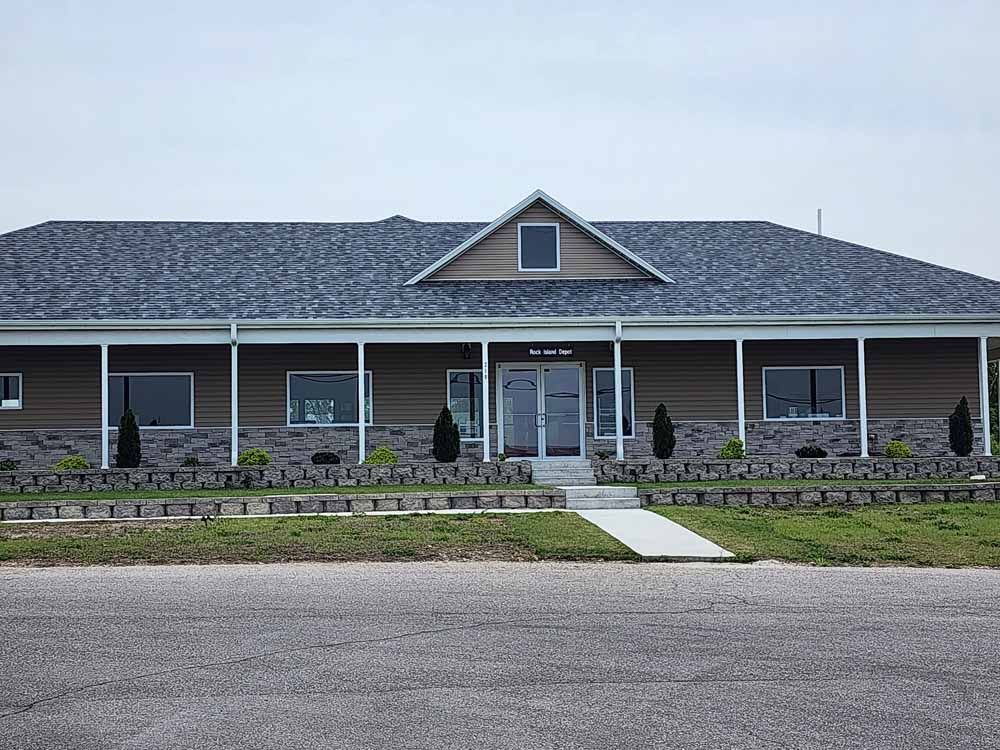 Brown and grey building with dark roof, windows, and small landscaping in front.