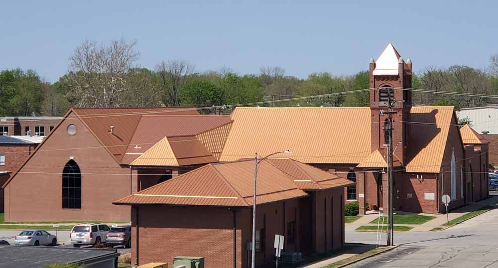 Red brick church with a copper-colored roof and steeple, under a blue sky.