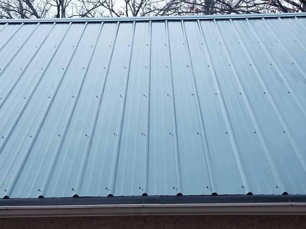 Metal roof with vertical ridges; light blue-gray color; visible screws; overcast sky.