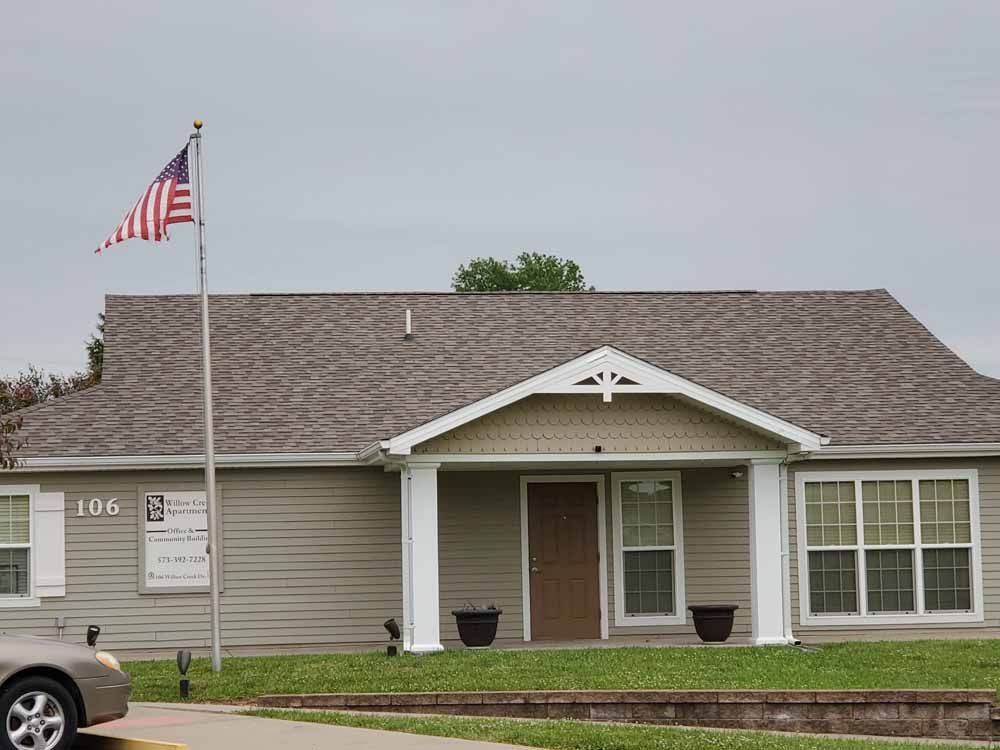A one-story building with the American flag in front. The building has a tan exterior and a brown roof.