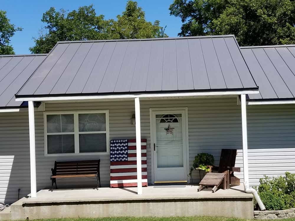 House with gray metal roof and porch, American flag art, and outdoor seating.