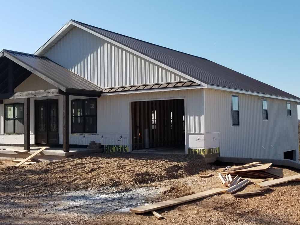 New house under construction with white siding, black roof, and garage opening.