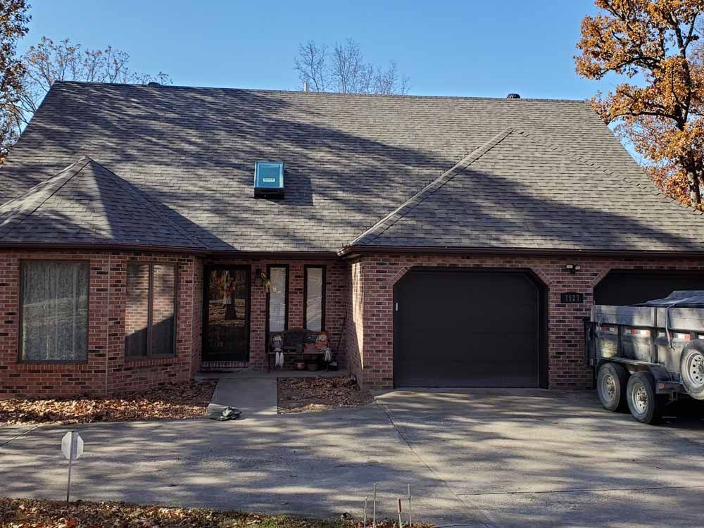 Brick house with dark roof and garage; trailer parked in driveway.