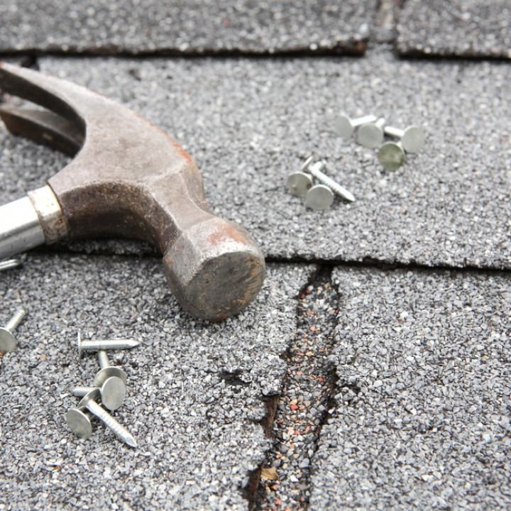 Hammer and nails on gray asphalt shingles, with a crack visible.