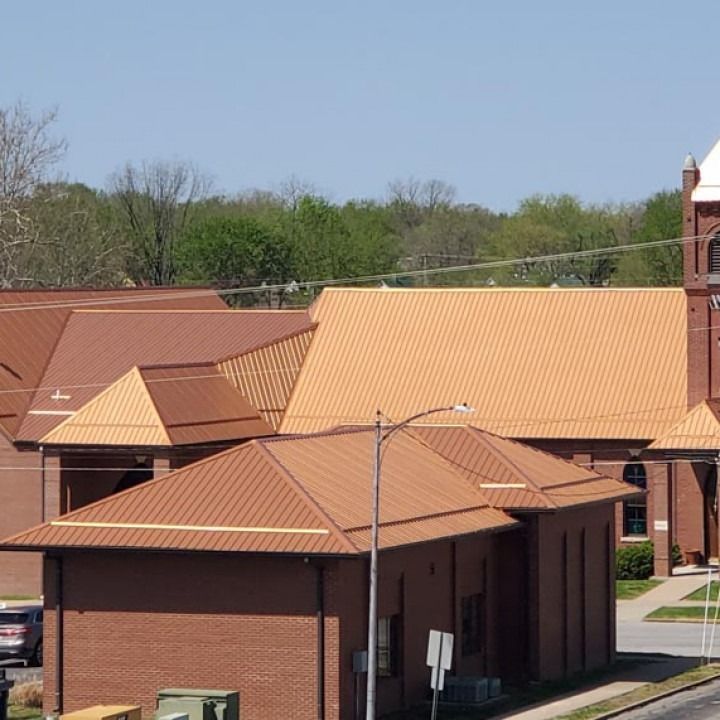 Brick building with copper-colored metal roofs against a backdrop of trees and a blue sky.
