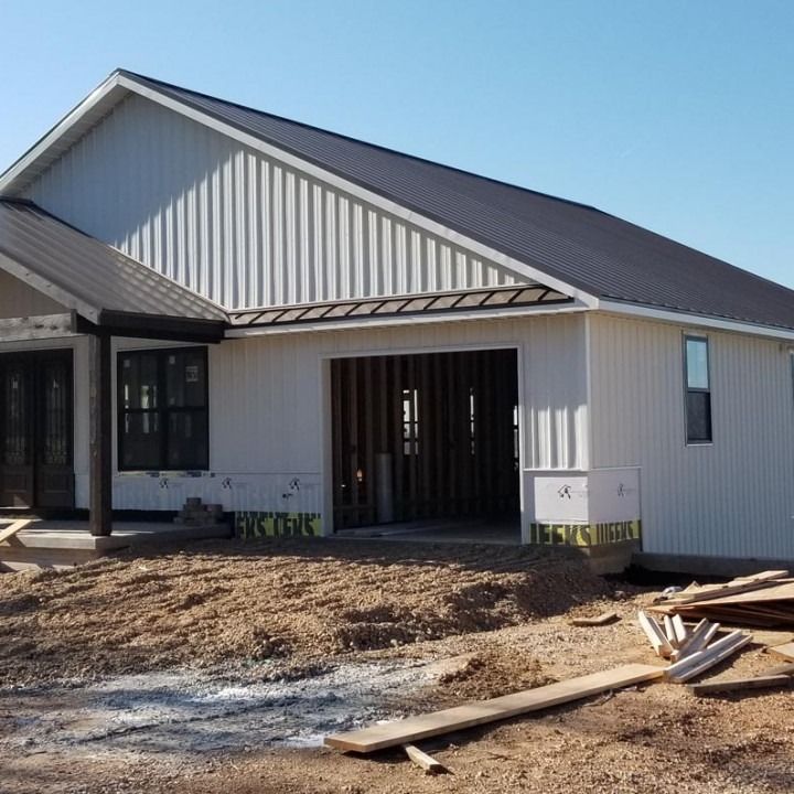 New construction home with white vertical siding, black metal roof, and an open garage.