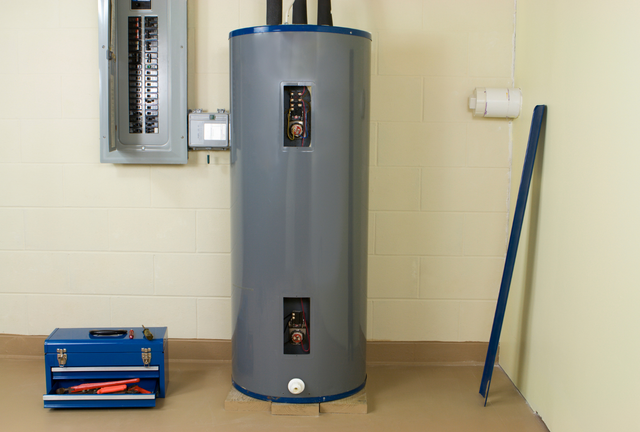 Gray water heater in a utility room, with a blue toolbox and broom against the wall.