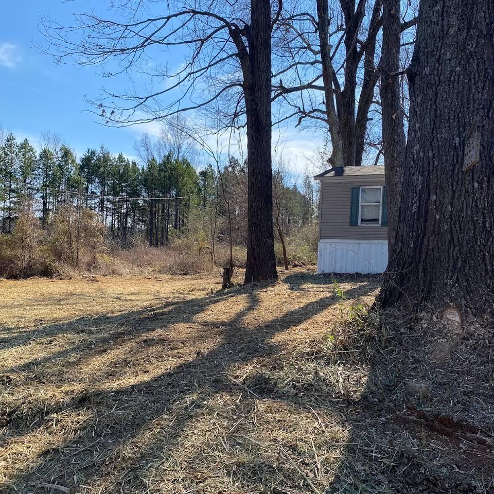 A small house is sitting in the middle of a field surrounded by trees.