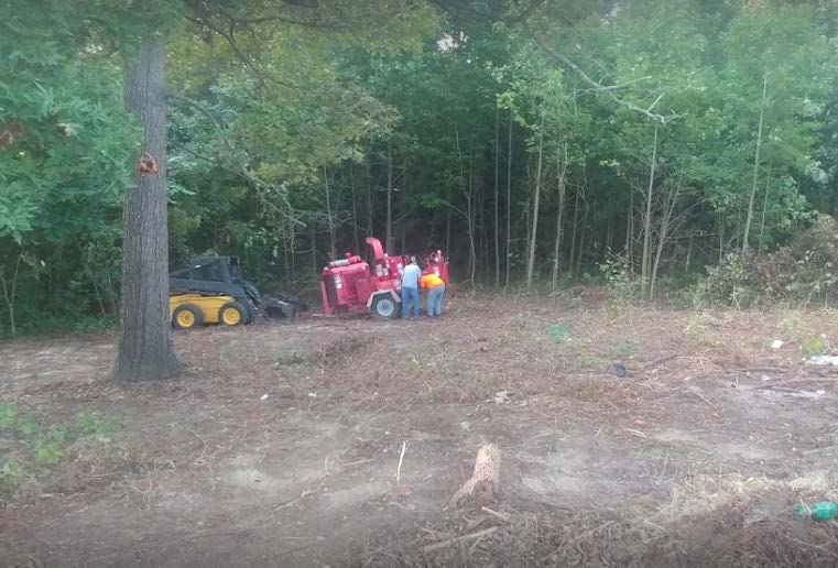 A group of people are standing next to a red machine in a field.