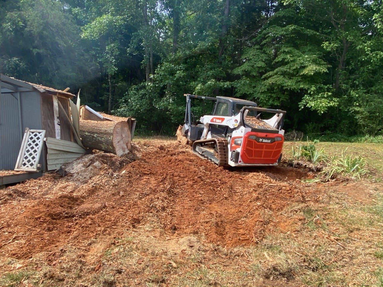 A bulldozer is moving dirt in a field next to a shed.