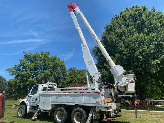 A white truck with a crane attached to it is parked in a grassy field.