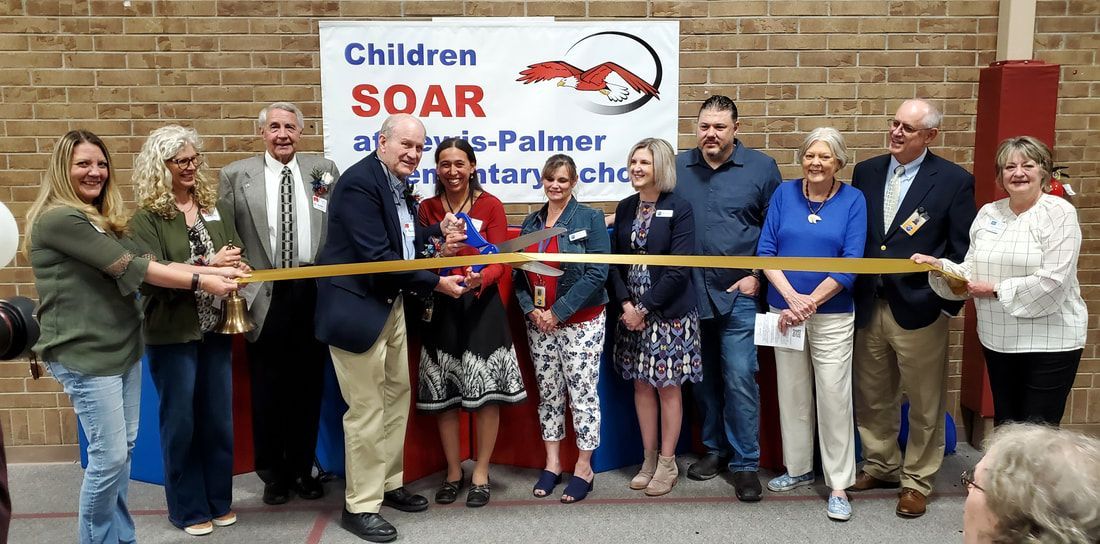 Group of people cutting a gold ribbon, with a sign reading 