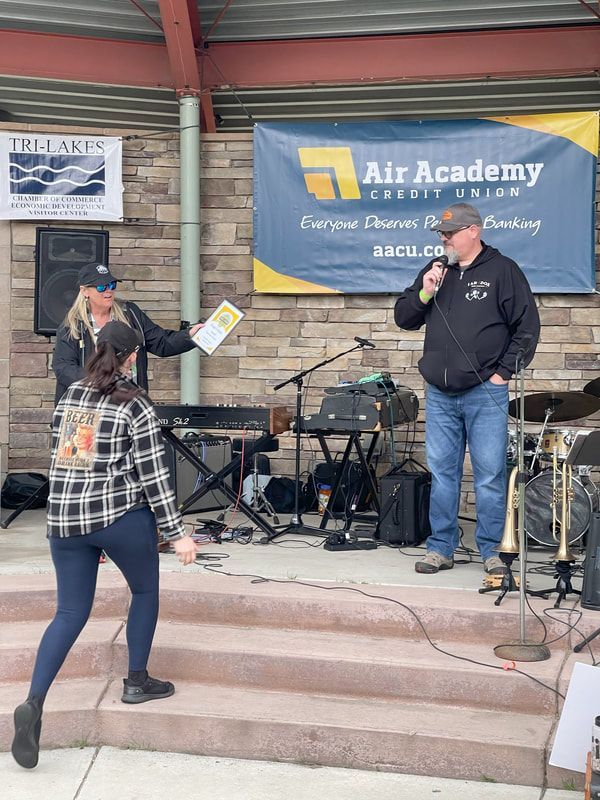 People on stage at event: man with microphone, woman presenting, band equipment. Banner: Air Academy Credit Union.