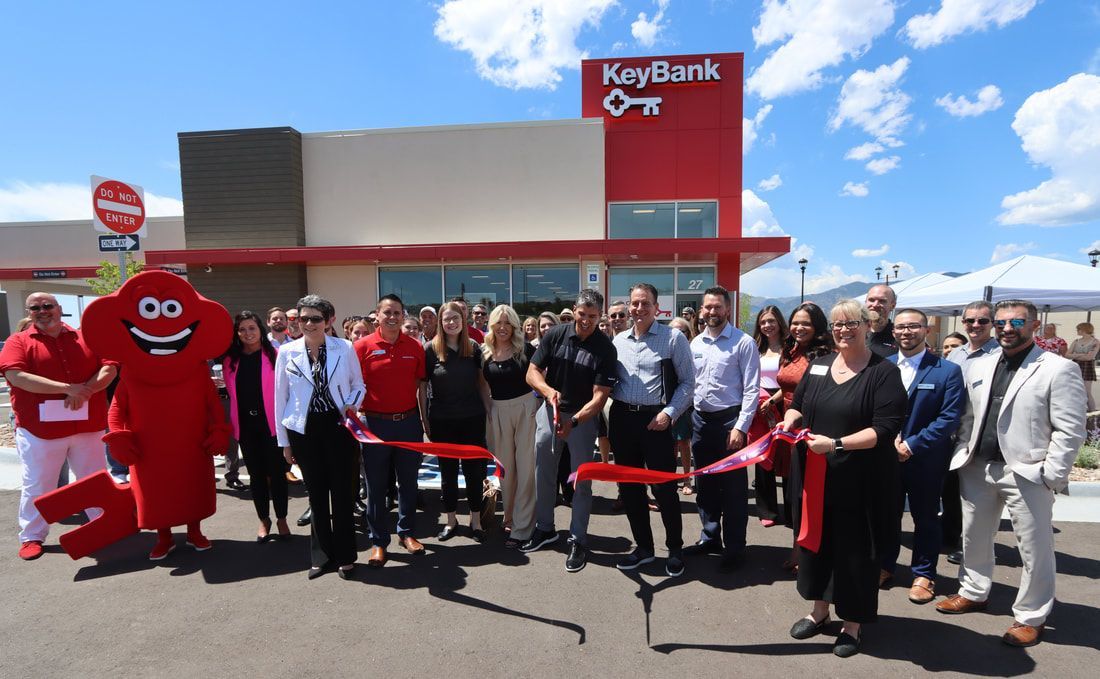 People at a KeyBank ribbon-cutting ceremony in front of the bank. Red accents, sunny day.