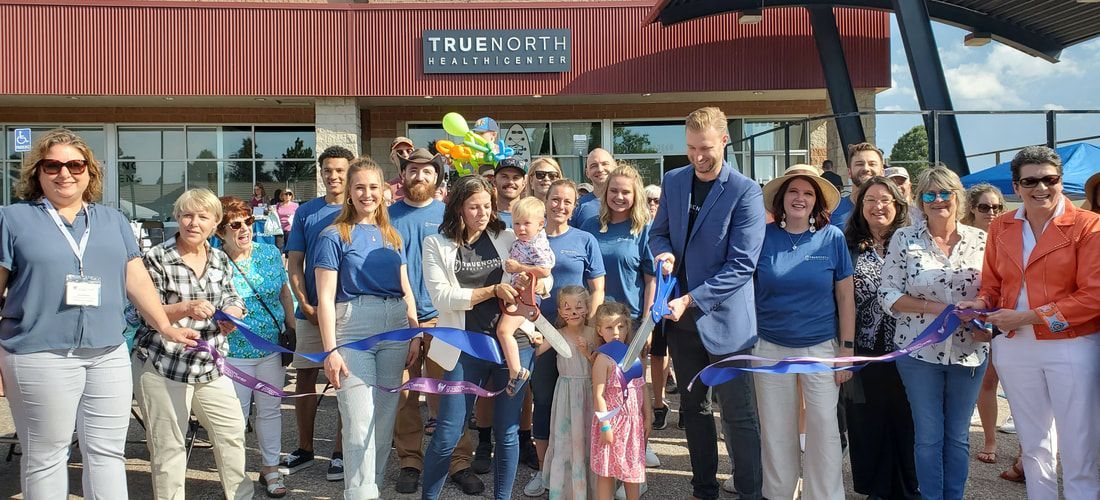 People cutting ribbon in front of a building with the sign 