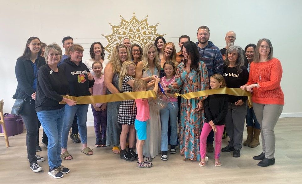 Group of people cutting a gold ribbon at a business opening.  A large mandala is on the wall.