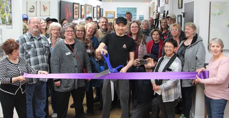 A group of people at a gallery opening, cutting a purple ribbon.