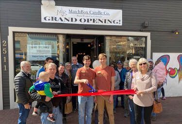 People at the grand opening of Matchbox Candle Co., cutting a ribbon outside a shop with a sign.