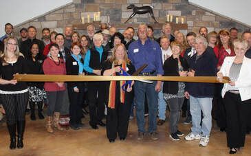 People cutting ribbon at a business opening, indoors. A statue sits above a stone fireplace.