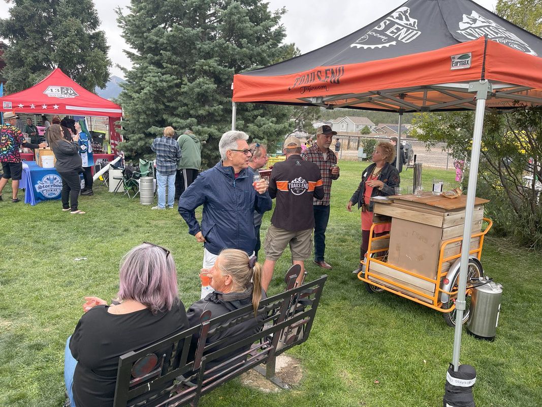 Outdoor event: People socializing near tents, a bench, and a beer cart.