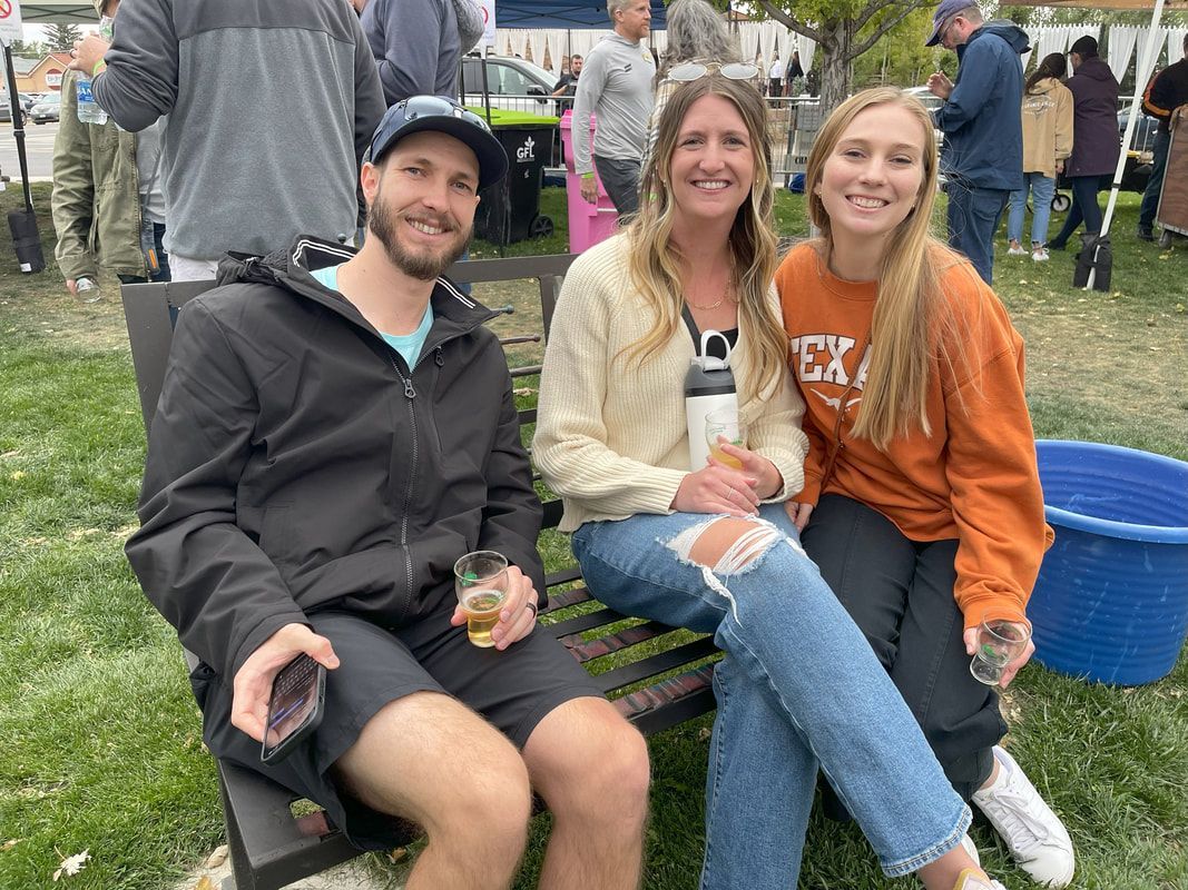 Three people, two women and a man, smiling and sitting together outdoors.