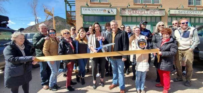A group of people at a ribbon-cutting ceremony, cutting a yellow ribbon in front of a building.