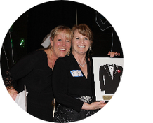 Two women smiling at a party; one holds a tuxedo drawing.