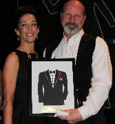 Woman and man holding framed tuxedo silhouette, smiling; formal event.