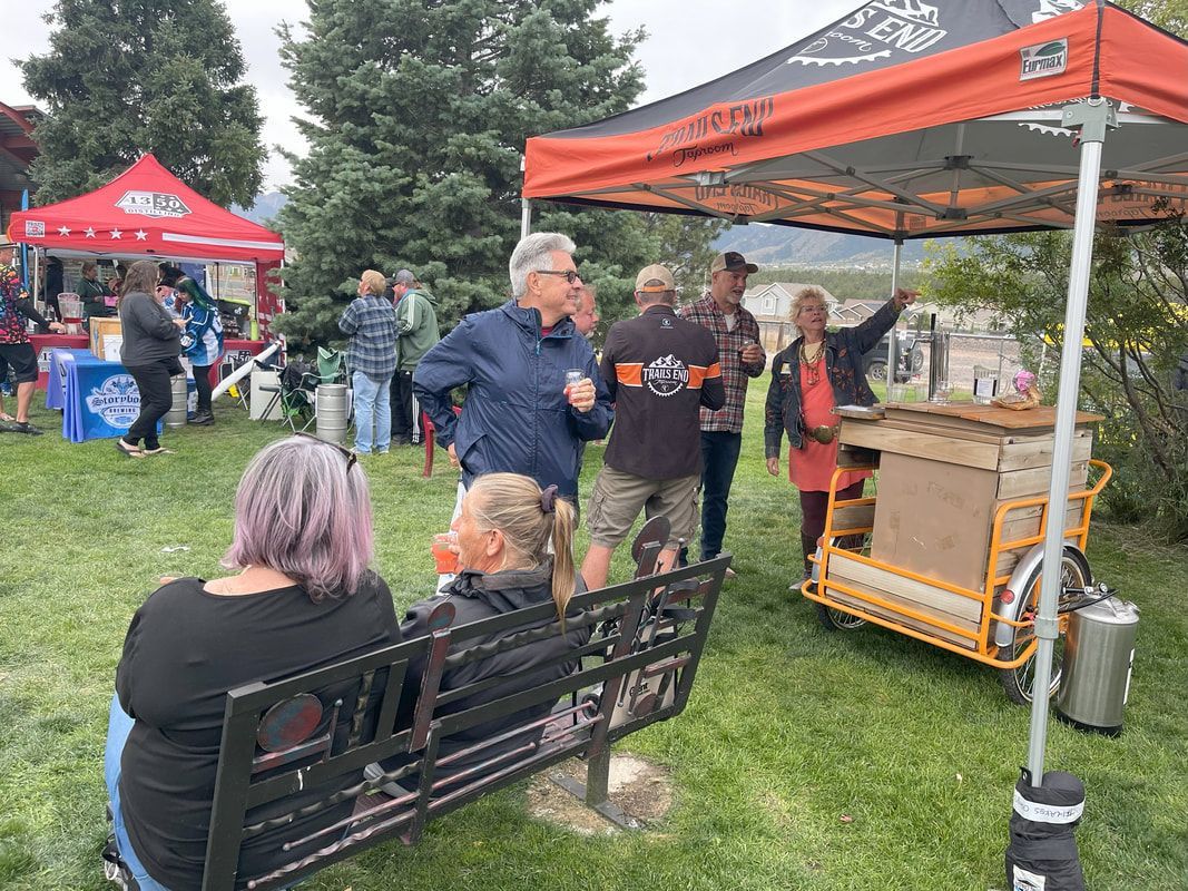 People at an outdoor event; food vendors, seated individuals, a tent, and trees on a cloudy day.