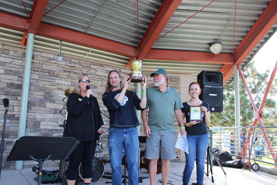 People on a stage holding trophies and a sign. A woman on the left speaks into a microphone.