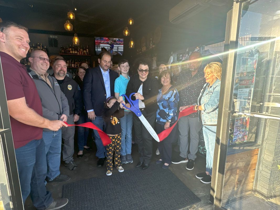 People cutting a red ribbon at a bar entrance, celebrating a grand opening.