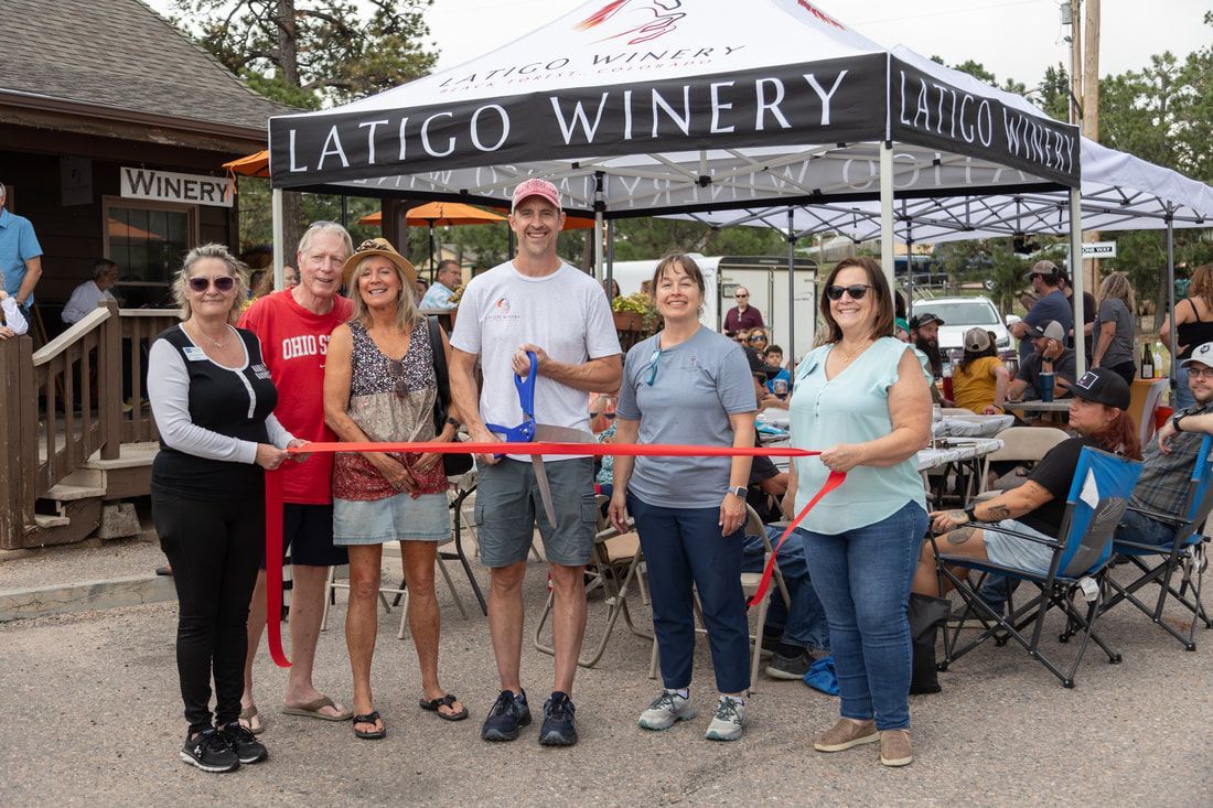 People cutting a ribbon at Latigo Winery's opening; several people smile; outdoor setting.