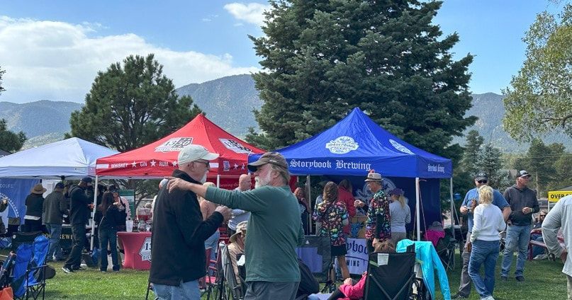 People gathered at outdoor event with tents, mountains in background. Men embracing.