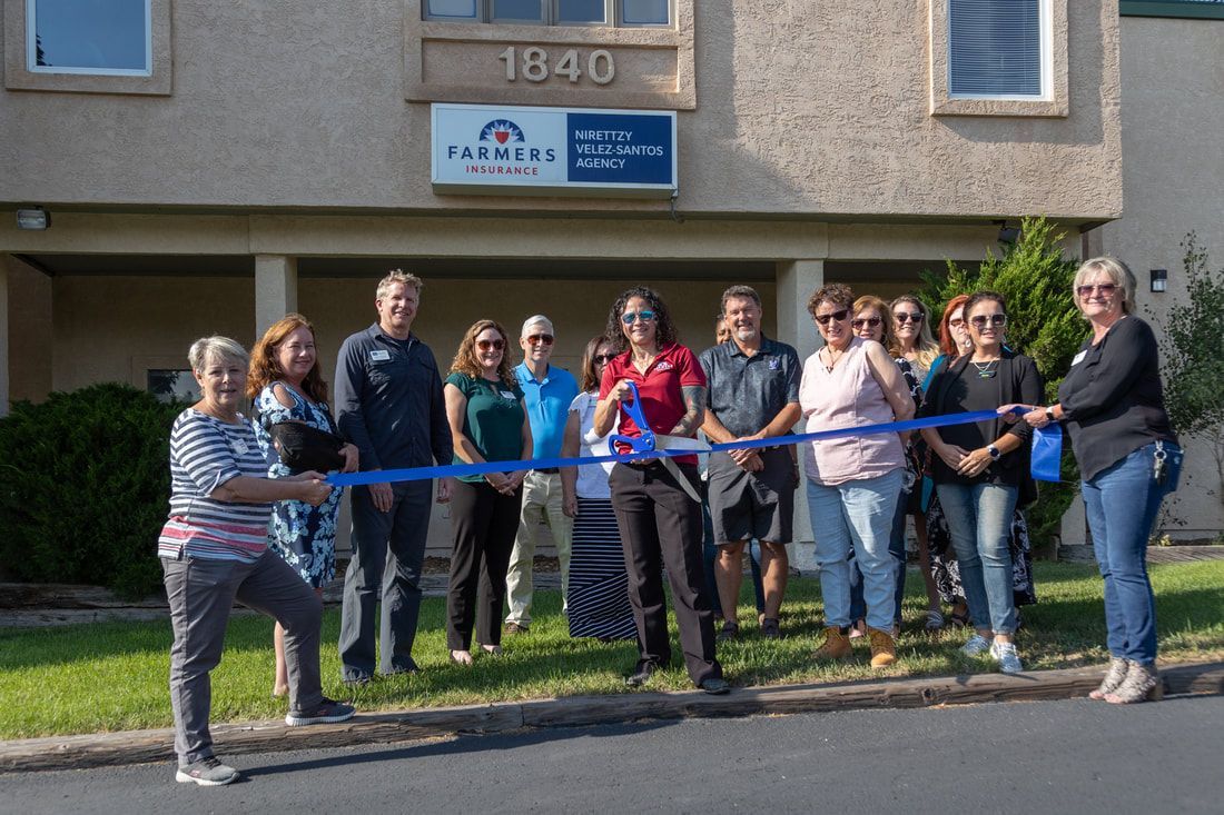 Group of people at a ribbon-cutting ceremony in front of a building, blue ribbon held, sunny day.