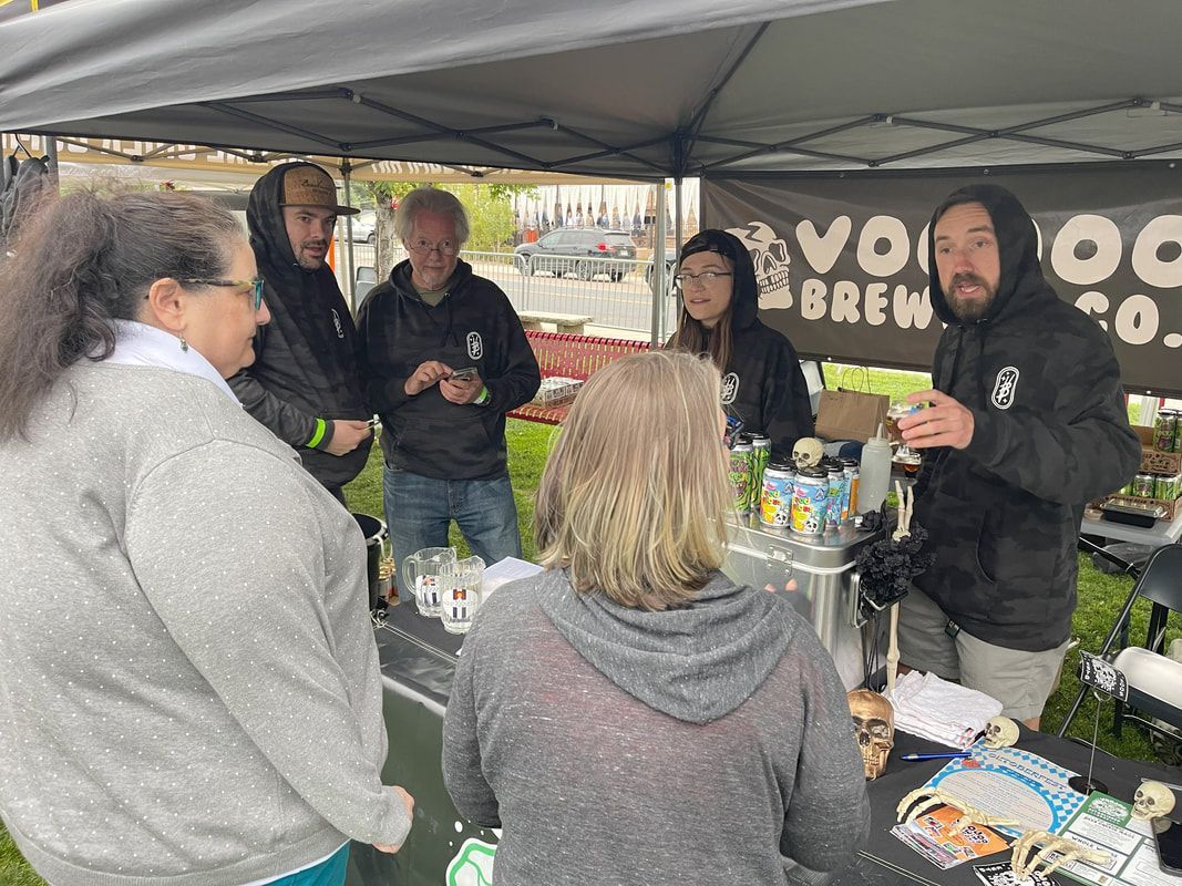 People at a Voodoo Brewery Co. booth. Several stand around a table, some tasting samples.