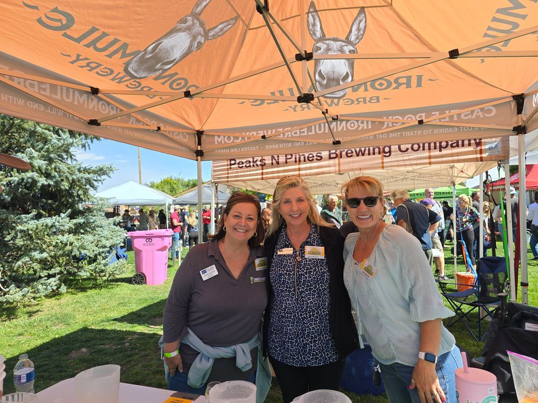 Three women smiling at an outdoor beer tent with a donkey logo.