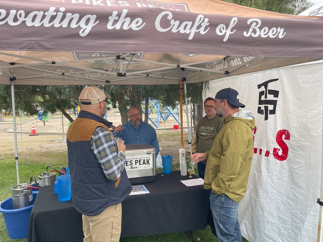 People at a beer tent. Men standing, one handing a drink. Brown tent, green grass, daytime.