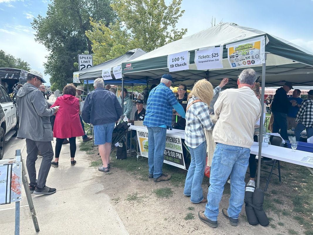 People at an outdoor event, gathered at a table under a tent.