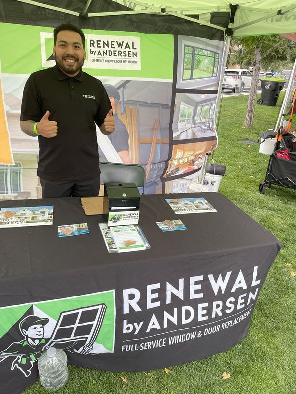 Man at Renewal by Andersen booth, smiling, giving thumbs up. Outdoor setting, green and black branding.