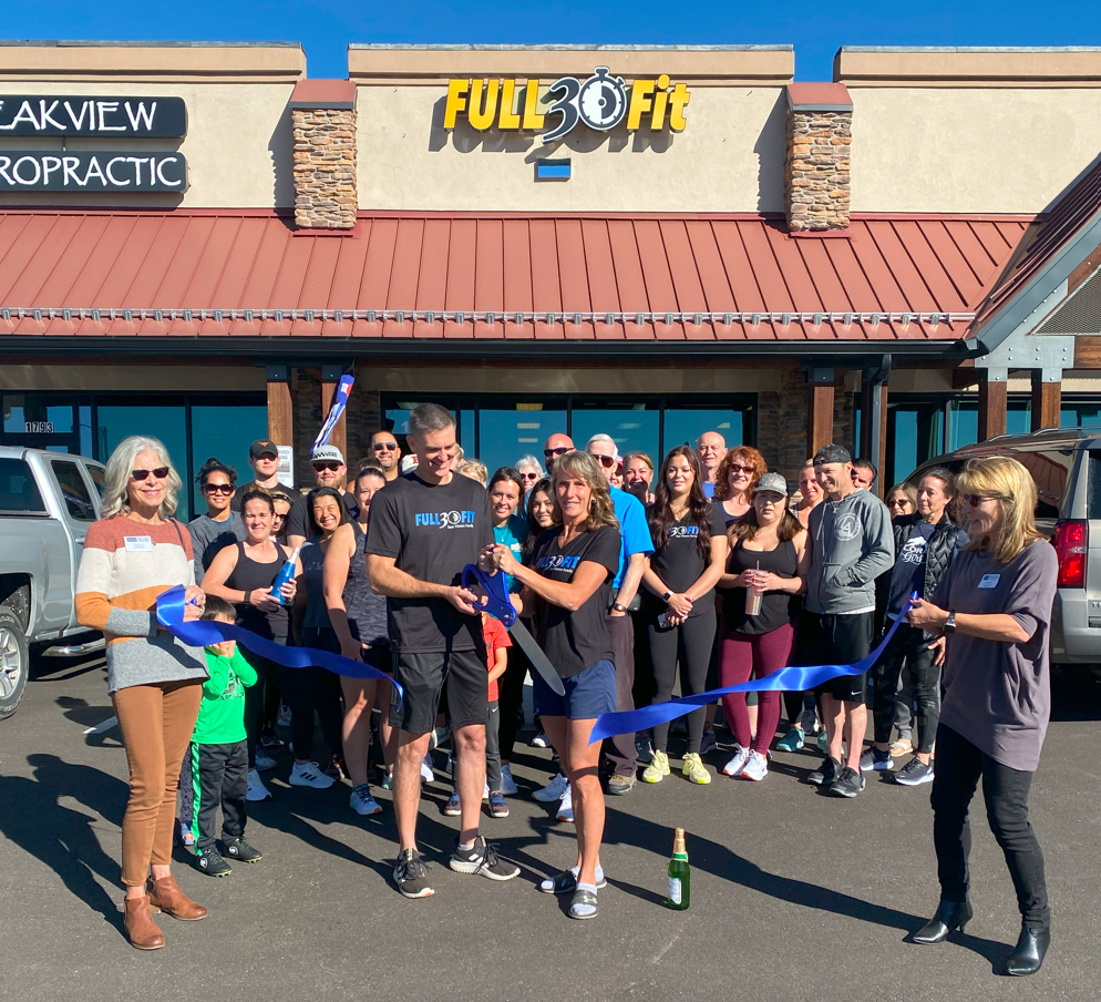 Ribbon-cutting at Full 2 Fit gym. People gather outside, holding ribbon. Building with signs.