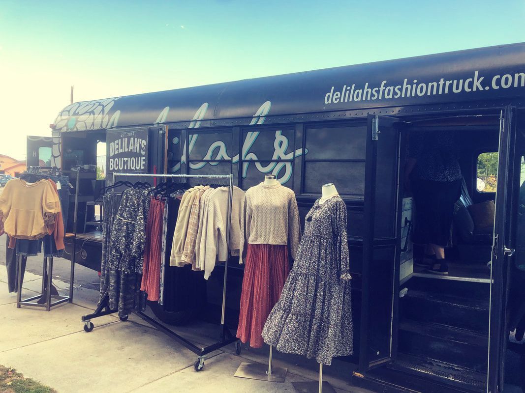 Fashion truck displaying clothing on racks and mannequins. Exterior with open door.